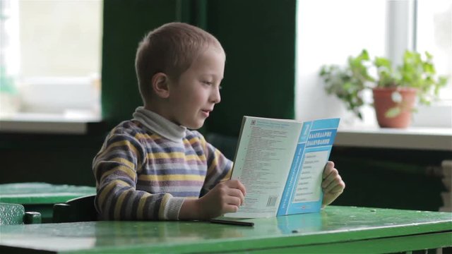 student at a desk reading a book/boy student reading a book in class