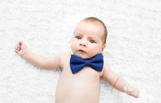 Cute baby with bow tie lying on white bedspread