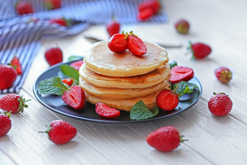 Plate with tasty pancakes and strawberries on wooden table