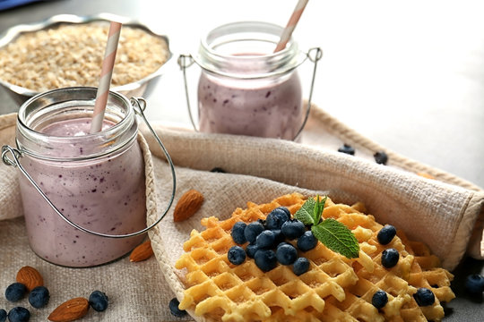 Two mason jars with tasty smoothie, wafers and some ingredients on blurred background