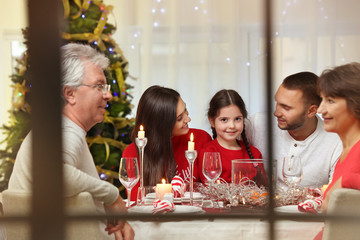 Happy family sitting at table served for Christmas dinner, view from window