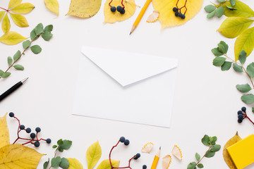 White empty envelope in autumn leaves frame. Paper cover on white background surrounded by yellow foliage and blueberry. Fall inspiration, good news, inbox concept