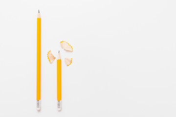 Long and short pencils with shavings on white background, free space for text or advertisement. Top view on two wood pencils with wooden flakes. Chancellery, art, drawing materials, design concept