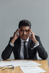 Depressed businessman sitting at the table with documents, looking at camera