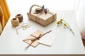 Fototapeta na wymiar Beautiful handmade gift box (package) with flowers, envelope with blank gift tag and decorative rope on white background. Wooden hart. Vintage Style. BOHO.
