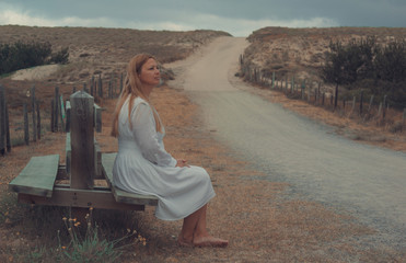 Caucasian woman sitting on a bench near the road leading to the sand dune on the southwest coast of France