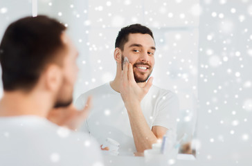 happy young man applying cream to face at bathroom