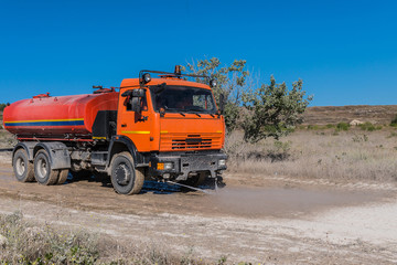 Fototapeta na wymiar Big orange street cleansing machine washes the dusty road