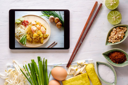 Tablet Showing Screen of padthai with Raw herb and Seasoning Prepare for Padthai on White Wooden Table Background.Thai traditional cusine.