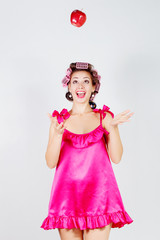 Girl in a nightgown and curlers catches hands red apple. Gray background.