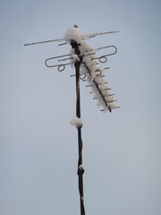 Snowy antenna on the roof against blue sky