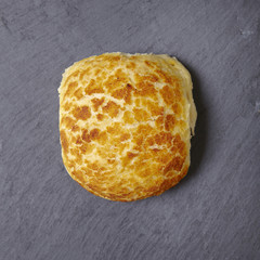 A single fresh baked bread roll on a rustic slate background