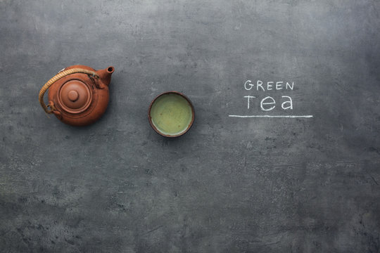 Fototapeta Green tea on kitchen table with chalky text. Top view on ceramic teapot and cup of tea.