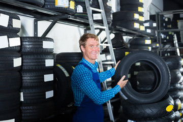 Smiling mechanic man standing with car tires