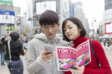 Obraz premium カップル 男女 東京観光 デート 渋谷スクランブル交差点 ガイドブックを手に スマホで検索