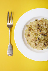 Aerial view of a dinner plate of chicken and mushroom risotto rice with fork on a bright yellow background