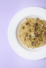 A dinner dish of chicken and mushroom risotto on a pastel purple colored background