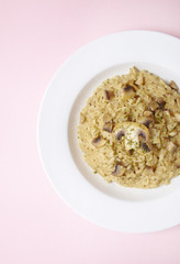 A dish of chicken and mushroom risotto on a pastel pink background