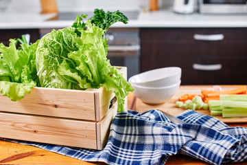 Lettuce in a wooden box in the background of chopped carrots and cucumber on a Board in the kitchen