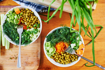 Top view of vegetable mix in bowls with green peas, cucumbers, carrots, lettuce and dill, standing on a wooden table