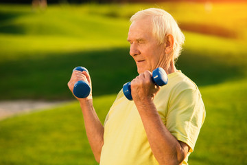Old man with dumbbells. Person doing exercise outdoor. Strengthen the muscles. Your health is priceless.
