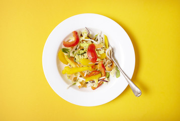 Aerial view of a bowl of fresh, chopped stir fry vegetables on a bright yellow background