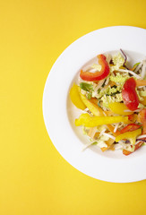 A bowl of fresh stir fry vegetables on a bright yellow background