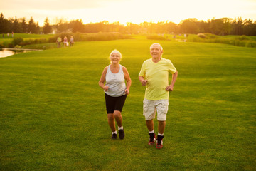 Obraz premium Couple jogging on grass. Senior man and woman smiling. Active leisure of pensioners. Save your health.