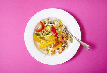 Aerial view of a bowl of fresh, chopped stir fry vegetables on a bright pink background