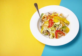 A bowl of fresh stir fry vegetables on a bright yellow and blue background forming a page border