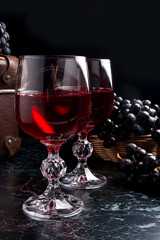Glass of red wine on dark marble background. Cluster of blue gra
