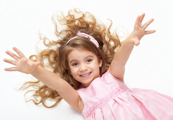 girl child with long hair lie on white and open arms, dressed in pink