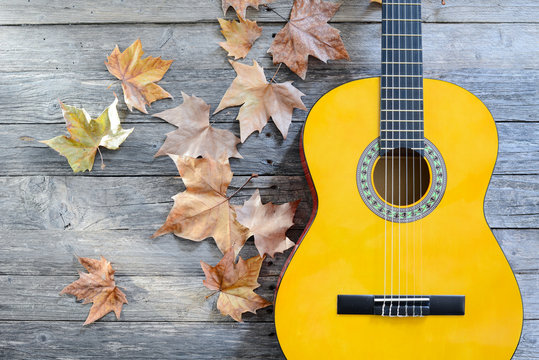 winter music symbol with autumn leaves and guitar on old wooden plank