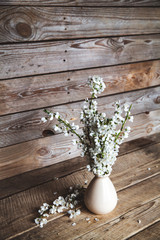 Vintage vase with cherry flowers on old wooden background.