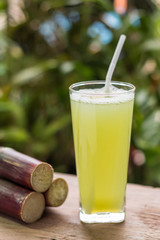 Sugarcane juice with piece of sugarcane on wooden background