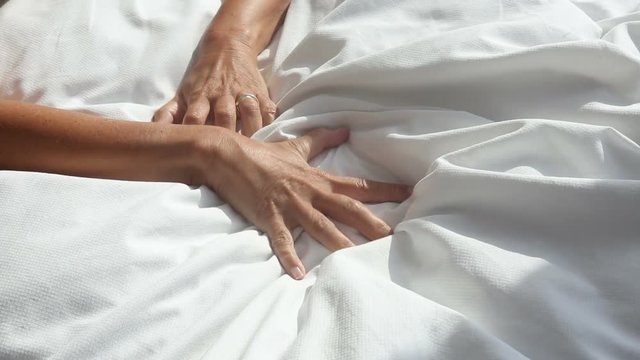 arms of woman grabbing a white blanket in bed and relaxes
