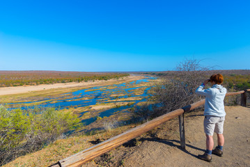 Fototapeta na wymiar Tourist looking at panorama with binocular from viewpoint over the Olifants river, scenic and colorful landscape with wildlife in the Kruger National Park, famous travel destination in South Africa.