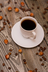 Small white cup of coffee, hazelnuts and cocoa beans on wooden background
