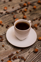 Small white cup of coffee, hazelnuts and cocoa beans on wooden background