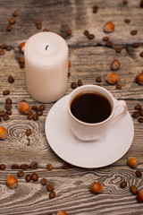 Small white cup of coffee, hazelnuts, cocoa beans, candle on wooden background