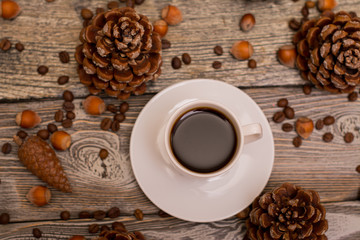 Small white cup of coffee, cocoa beans, hazelnuts, cone on wooden background