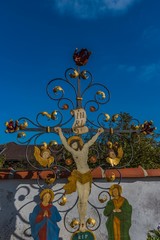 Buntes Grabkreuz aus Schmiedeeisen vor blauem Himmel