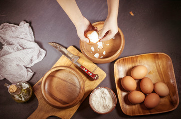 Girl's hands is shelling chicken eggs. Stuffing for home-made pie. Boiled chicken eggs in wooden ware on a dark table. Vintage toning