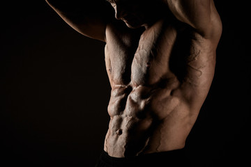 torso of attractive male body builder on black background.