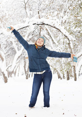 Fototapeta na wymiar Happy beautiful girl in knitted hat and blue winter jacket, rejoices in park outdoor, full length