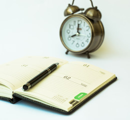 Day timer organizer with a pen and a mechanical alarm clock, time management and activity planning concept, busy schedule organization, selective focus