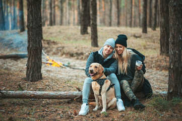 Romantic couple with dog sitting near bonfire, autumn forest background. Young blonde woman and handsome man. Concept - family, togetherness, love, friendship.