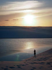 Fototapeta premium A solitary man enjoying a moment alone among the lagoons and sand dunes of the Lençóis Maranhenses National Park - Barreirinhas, Maranhão, Brazil.