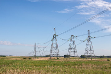 Powerful line of electricity transmission poles stand in a field on a background of nature and the sky with a view into the distance. The high-voltage cable