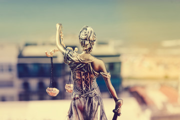 Back view of Lady Justice, statuette of the Themis goddess. Law concept. City buildings outdoor...